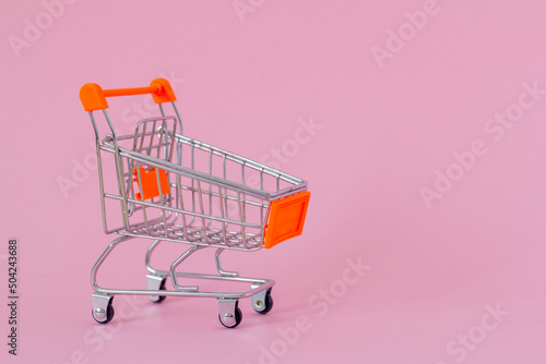 Shopping cart on pink background with copy space.