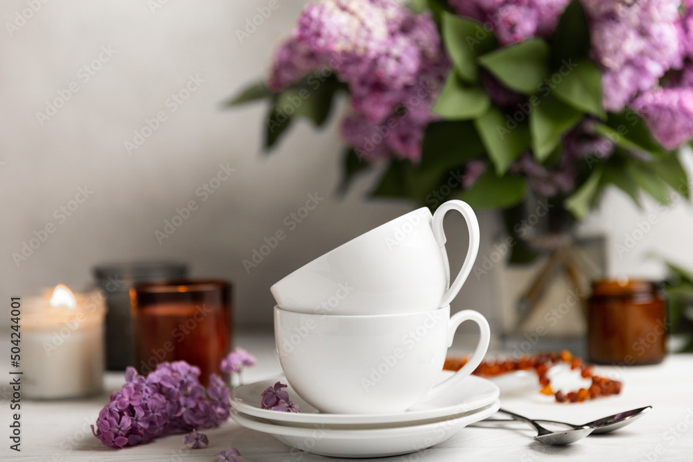 Tea set against the background of a spring bouquet of lilacs on a textured gray background. Composition with books and candles. Side view. Place to copy. Tea set against the background of a spring bouquet of lilacs on a textured gray background. Composition with books and candles. Side view. Place to copy.