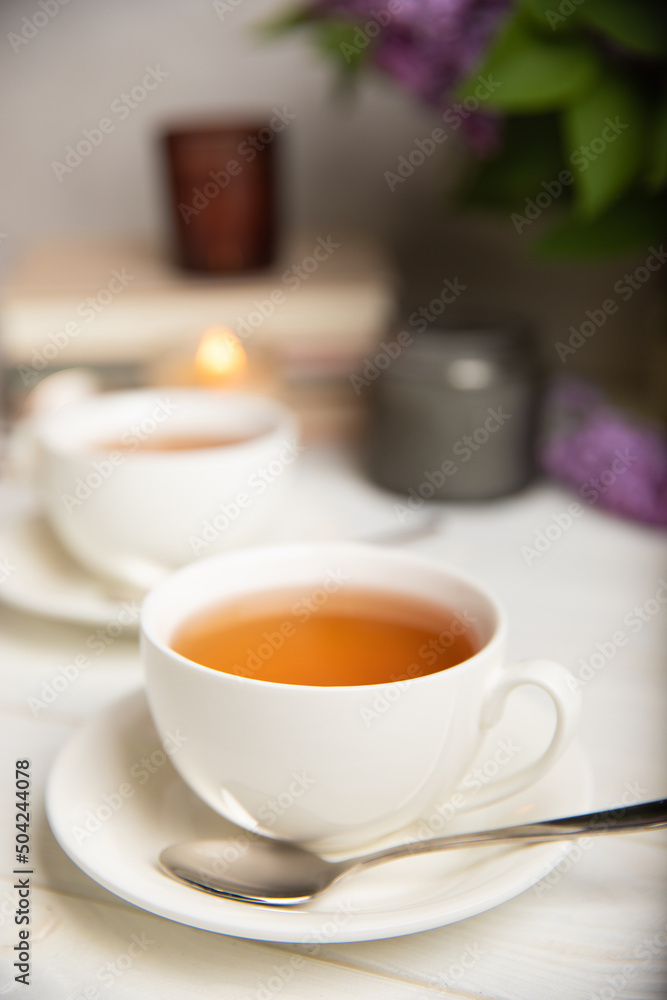 A cup of green tea against the background of a spring bouquet of lilacs on a textured gray background.Romantic composition with books and candles. Spring tea drink. Side view. Place to copy. A cup of green tea against the background of a spring bouquet of lilacs on a textured gray background.Romantic composition with books and candles. Spring tea drink. Side view. Place to copy.