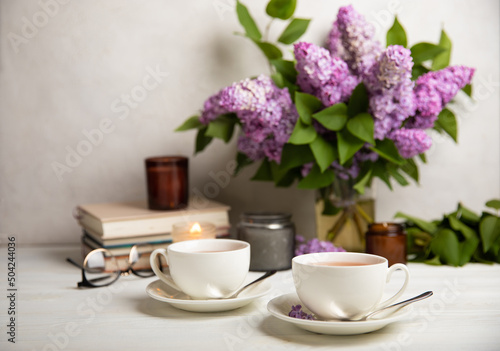 A cup of green tea against the background of a spring bouquet of lilacs on a textured gray background.Romantic composition with books and candles. Spring tea drink. Side view. Place to copy.