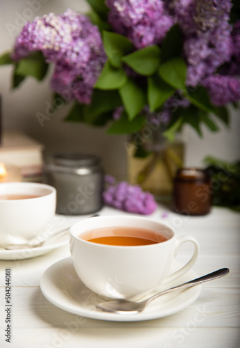 A cup of green tea against the background of a spring bouquet of lilacs on a textured gray background.Romantic composition with books and candles. Spring tea drink. Side view. Place to copy.