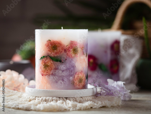 Handmade candles of a unique design, with different flowers, dry leaves on a light background. Candles made from organic wax, paraffin wax. Relaxation atmosphere. Luxurious lifestyle.