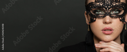 Beautiful young woman in black mysterious venetian mask on black banner background. Fashion photo