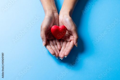 Fototapeta Naklejka Na Ścianę i Meble -  Cropped hands of african american mid adult woman holding red heart shape on blue background