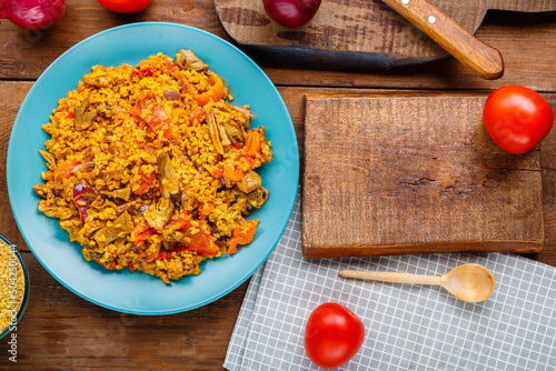 A large dish of bulgur with vegetables and mushrooms in spices on the table on a blue napkin next to tomatoes and onions.