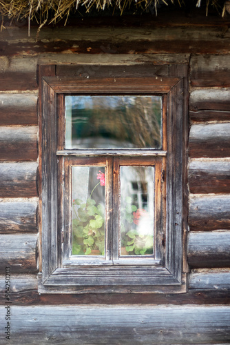 Window in an old log house. View of a fragment of a wall of a wooden building with a window. Reflection in the glass of an old window. Lonely window on the wall made of logs close-up.