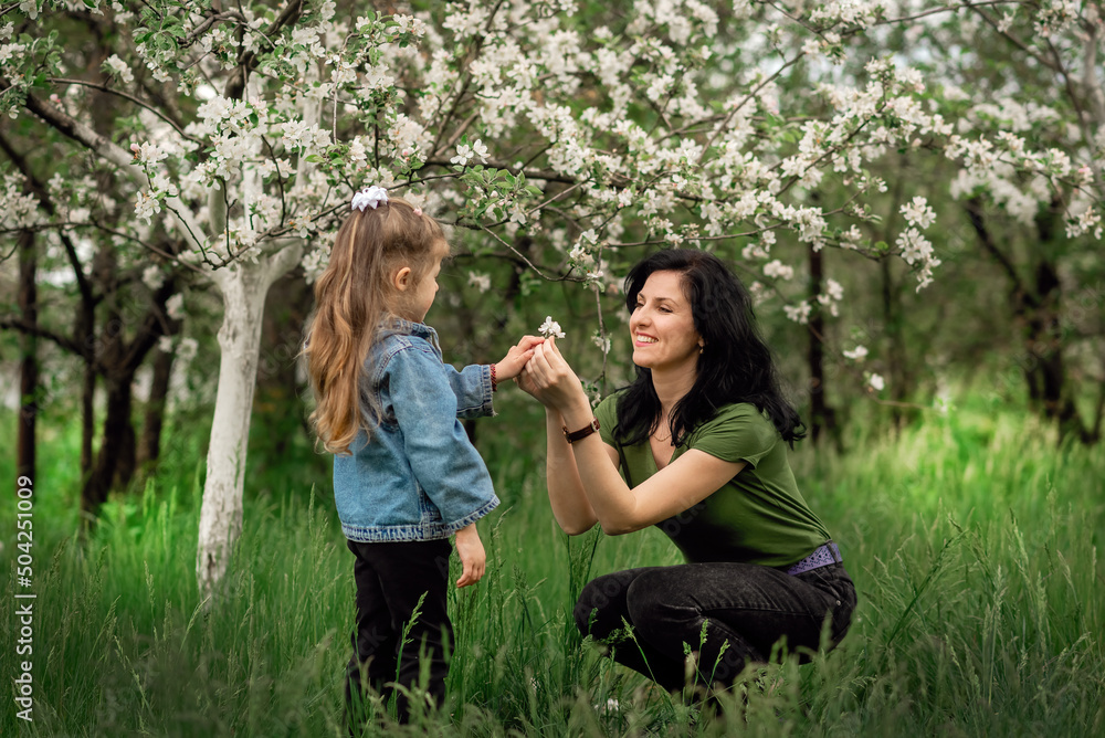 Mother and daughter are looking at each other and smiling in a blooming apple orchard Mother and daughter are looking at each other and smiling in a blooming apple orchard