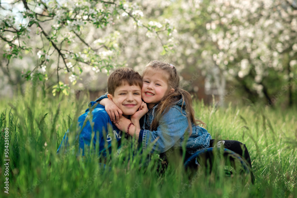 Fototapeta premium brother and sister are sitting and hugging in a blooming apple orchard