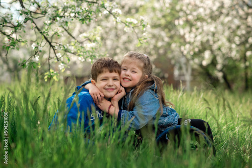 brother and sister are sitting and hugging in a blooming apple orchard