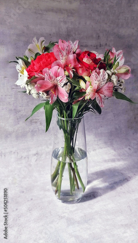 Bouquet of beautiful flowers, with roses in a transparent vase, on a gray background. © AlexaWork