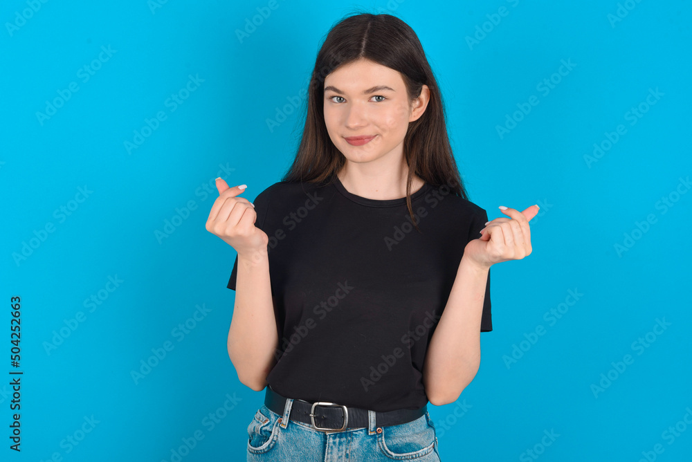 young caucasian woman wearing black T-shirt over blue background , making money gesture. young caucasian woman wearing black T-shirt over blue background , making money gesture.