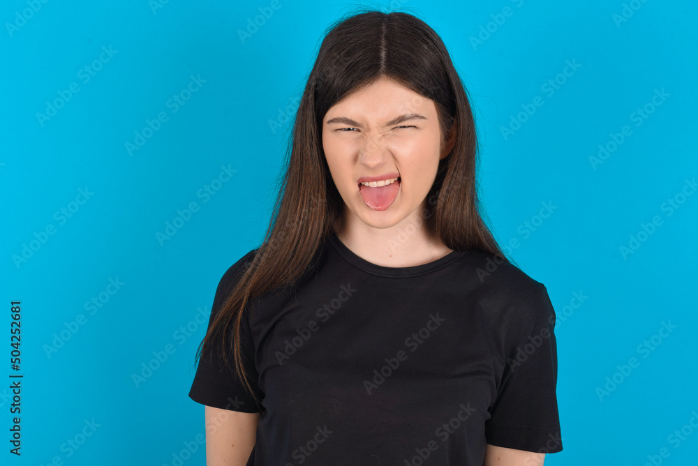 Body language. Disgusted stressed out young caucasian woman wearing black T-shirt over blue background , frowning face, demonstrating aversion to something. Body language. Disgusted stressed out young caucasian woman wearing black T-shirt over blue background , frowning face, demonstrating aversion to something.