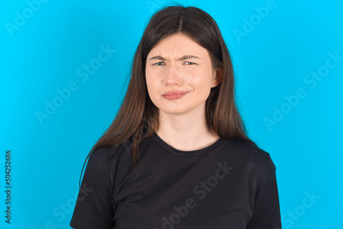 young caucasian woman wearing black T-shirt over blue background being nervous and scared biting lips looking camera with impatient expression, pensive.