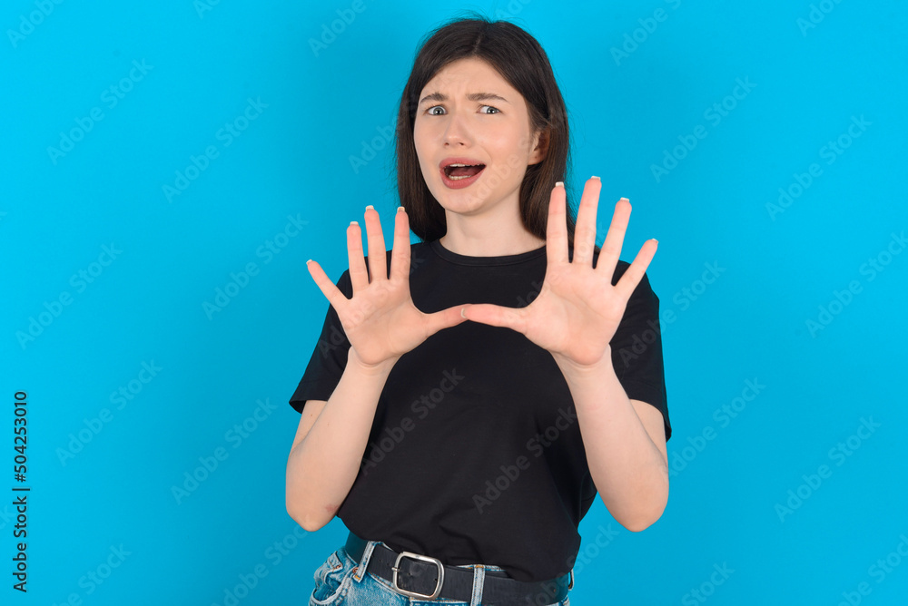 Dissatisfied young caucasian woman wearing black T-shirt over blue background frowns face, has disgusting expression, shows tongue, expresses non compliance, irritated with somebody. Dissatisfied young caucasian woman wearing black T-shirt over blue background frowns face, has disgusting expression, shows tongue, expresses non compliance, irritated with somebody.
