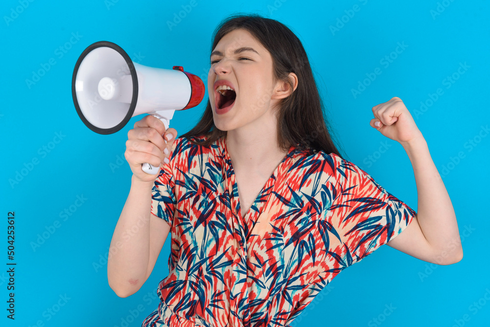 young caucasian woman wearing floral dress over blue background communicates shouting loud holding a megaphone, expressing success and positive concept, idea for marketing or sales. young caucasian woman wearing floral dress over blue background communicates shouting loud holding a megaphone, expressing success and positive concept, idea for marketing or sales.