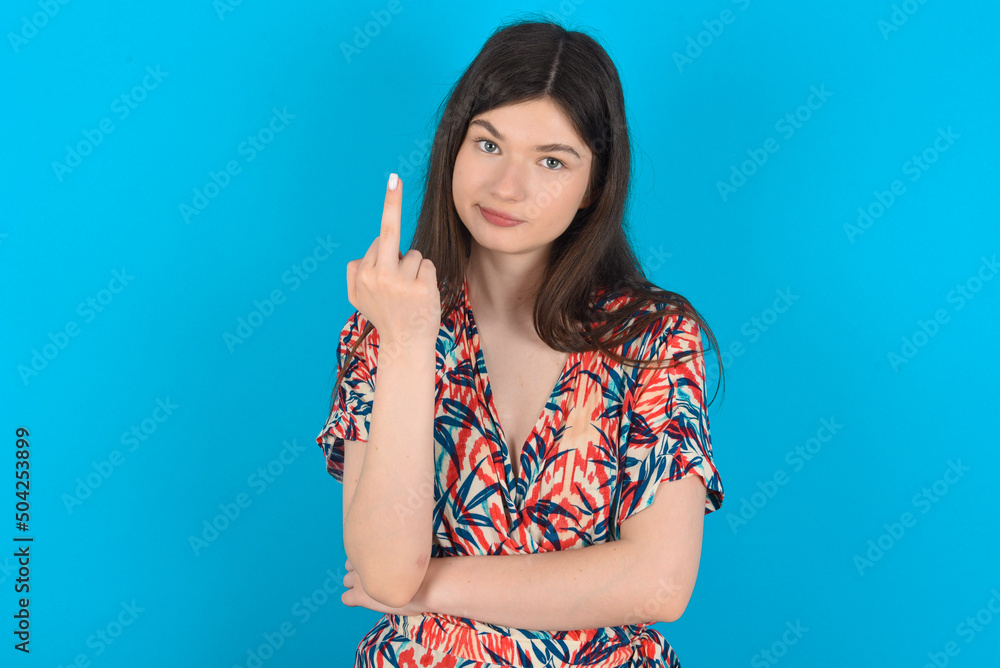 young caucasian woman wearing floral dress over blue background shows middle finger bad sign asks not to bother. Provocation and rude attitude. young caucasian woman wearing floral dress over blue background shows middle finger bad sign asks not to bother. Provocation and rude attitude.