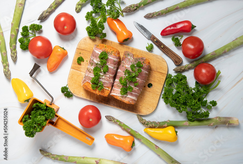 minced meat sausages in bacon with green parsley and fresh vegetables, peppers