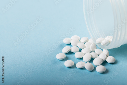 Close-up of white medicines spilled from bottle over blue background, copy space