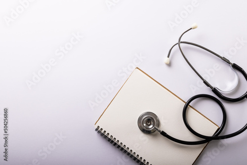 Directly above shot of blank spiral notebook with stethoscope on white background, copy space