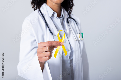 Midsection of african american mid adult female doctor holding yellow sarcoma awareness ribbon photo