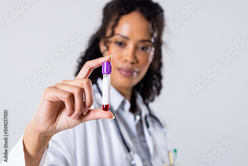 African american mid adult female doctor holding blood sample in test tube against white background