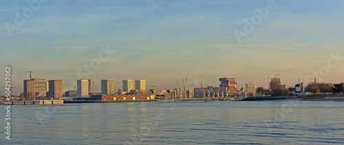 Old warehouses with industrial cranes and new residential skyscrapers along river Scheldt in Anwerp in warm evening light photo