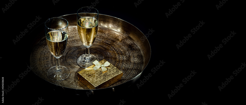Zwei Sektgläser mit Geschenk auf goldenem Tablett und schwarzem Hintergrund