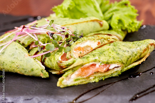 spinach rolls with salmon and microgreens on a black ceramic