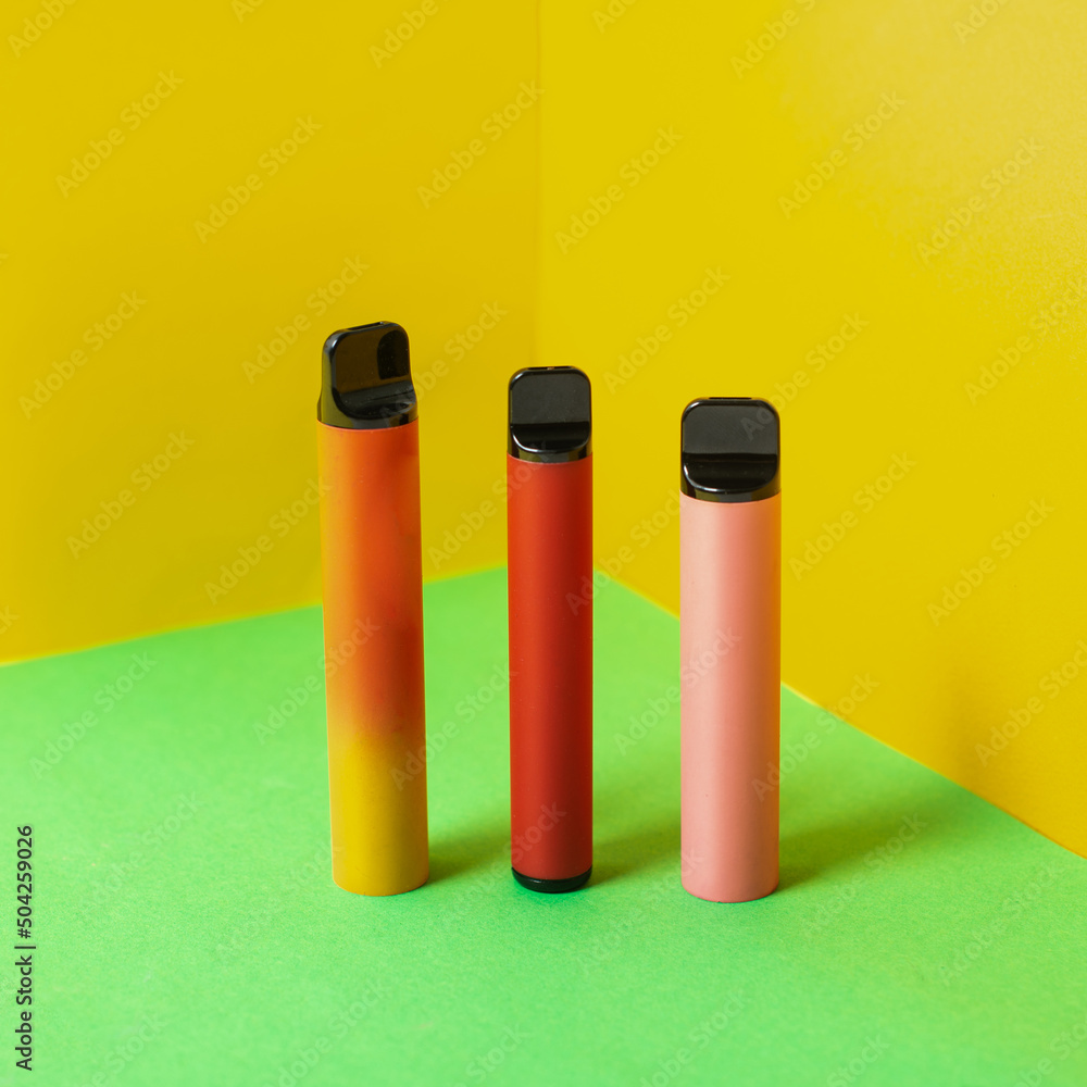 Colorful disposable electronic cigarettes with shadows on a yellow background. The concept of modern smoking, vaping and nicotine. Colorful disposable electronic cigarettes with shadows on a yellow background. The concept of modern smoking, vaping and nicotine.