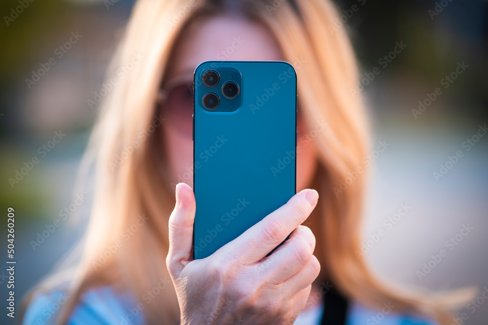 Woman holding a blue phone in her hands and photographs. Back side of the phone