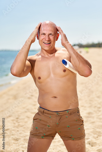 Handsome sexy man relaxing near hotel pool applying sunscreen cream. Summer vacation sea sun tan concept