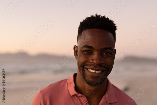 Close-up portrait of smiling african american young man at beach against clear sky during sunset