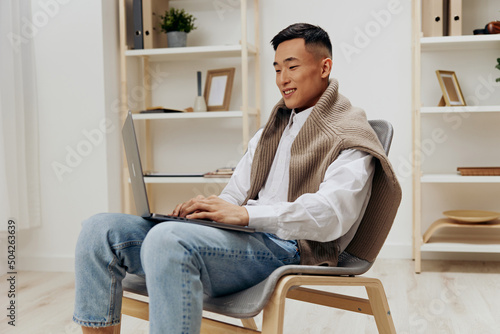 Asian man home with laptop in chair interior internet isolated background © SHOTPRIME STUDIO