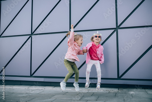 Two little girls wearing stylish pink clothes, having fun outdoors. © polinaloves