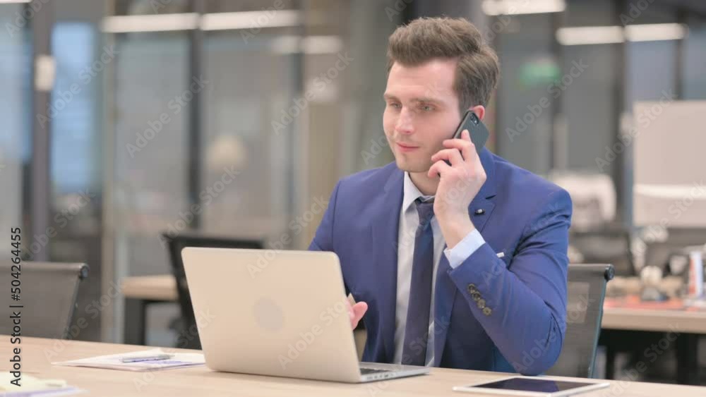 Businessman Talking on Phone while using Laptop in Office Businessman Talking on Phone while using Laptop in Office