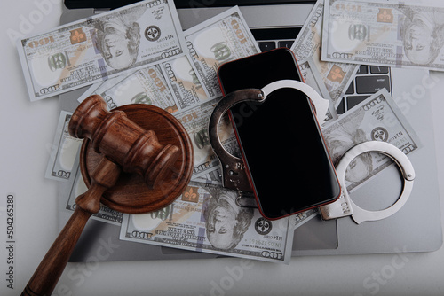 Top view of smartphone with handcuff on a dollar banknotes and laptop. Cyber crime and law concept