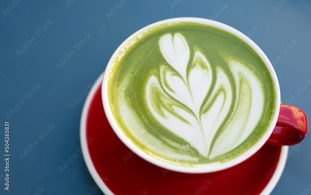 Cup of matcha latte in red cup on blue background in a cafe with copy space. High quality photo. Cup of matcha latte in red cup on blue background in a cafe with copy space. High quality photo.