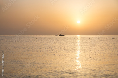 Small ship with boat and orrange disk of the sun setting over the sea during sunset on the Mediterranean sea, Turkey, Antalya Province