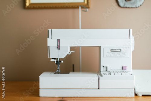 White simple sewing machine set up at a home office desk.