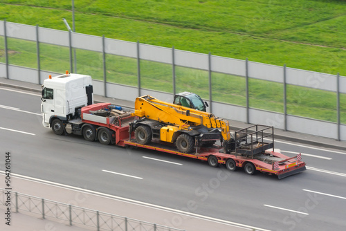 A truck transports a car lift with a cradle on a platform trailer along the highway.