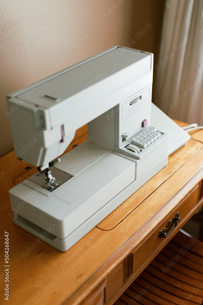 White simple sewing machine set up at a home office desk.