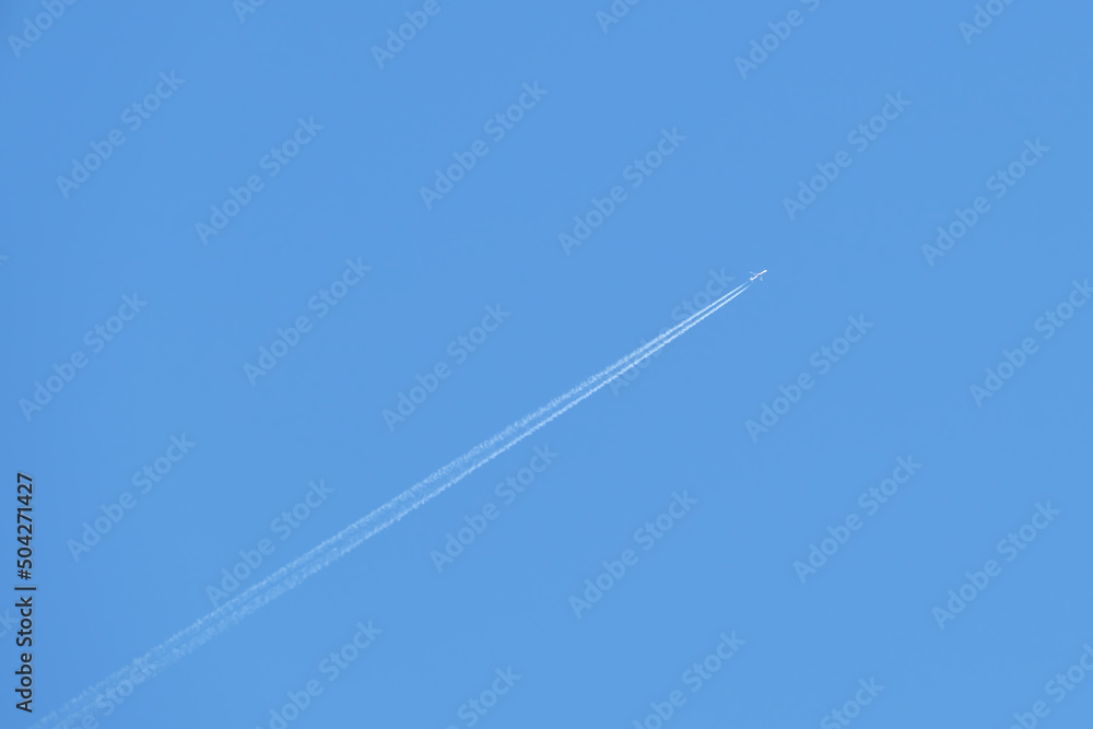 Distant passenger jet plane flying on high altitude on clear blue sky leaving white smoke trace of contrail behind. Air transportation concept Distant passenger jet plane flying on high altitude on clear blue sky leaving white smoke trace of contrail behind. Air transportation concept