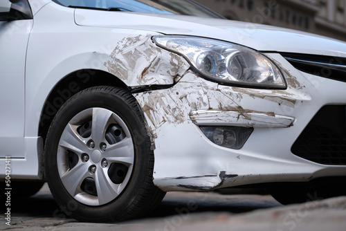 Dented car with damaged fender parked on city street side. Road safety and vehicle insurance concept © bilanol