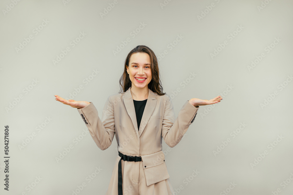 Puzzled woman in smart casual clothes stands on a beige background and spreads her arms away from confusion, looks at the camera, wears a beige suit. Puzzled woman in smart casual clothes stands on a beige background and spreads her arms away from confusion, looks at the camera, wears a beige suit.