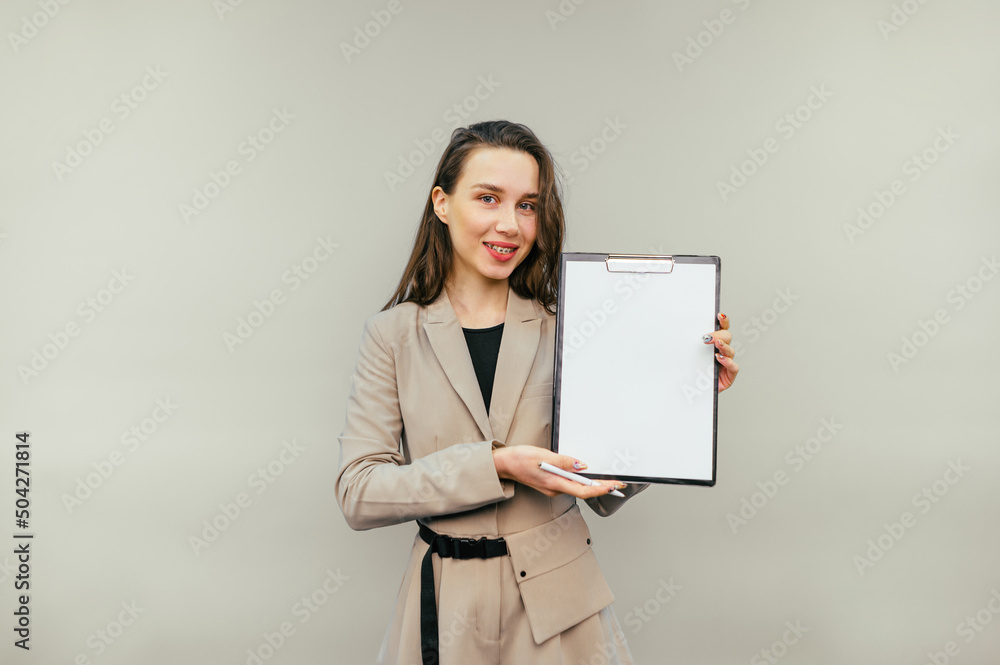 Positive business woman holding a tablet with a blank white sheet in her hand and looking at the camera with a smile on her face. Positive business woman holding a tablet with a blank white sheet in her hand and looking at the camera with a smile on her face.