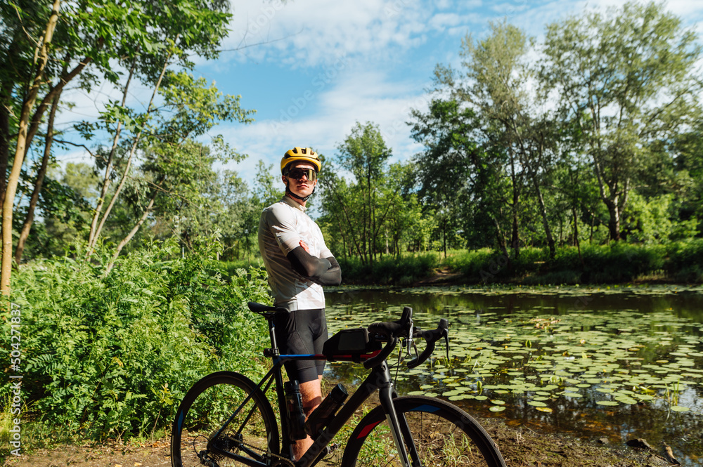 Obraz premium Male professional cyclist stands on the river bank outside the city with a bicycle and poses for the camera