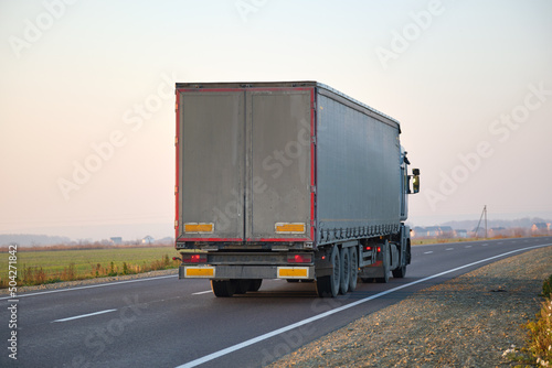 Semi-truck with cargo trailer driving on highway hauling goods in evening. Delivery transportation and logistics concept