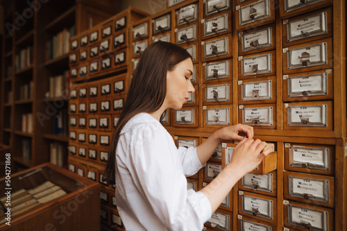 Attractive woman in a white blouse searches for information in the archives of the public library, opens a drawer.