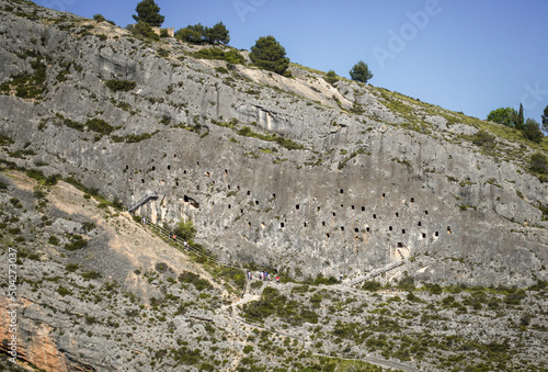 Covetes dels Moros Cave Holes in Rock Mountain Front View in Bocairent Medieval Village with Tourists at the Entrance during the Day. Rural Tourism Concept in Valencia Spain photo