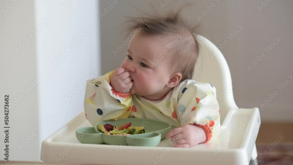 An infant 7-month caucasian girl is eating pasta with bare hands An infant 7-month caucasian girl is eating pasta with bare hands